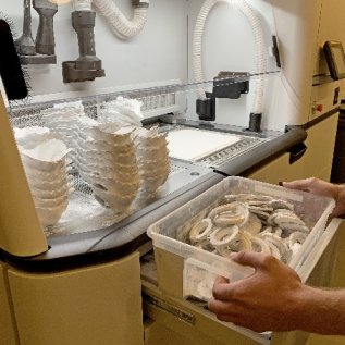 Operátor 3D tiskárny z ní vyndává vytištěné respirátory