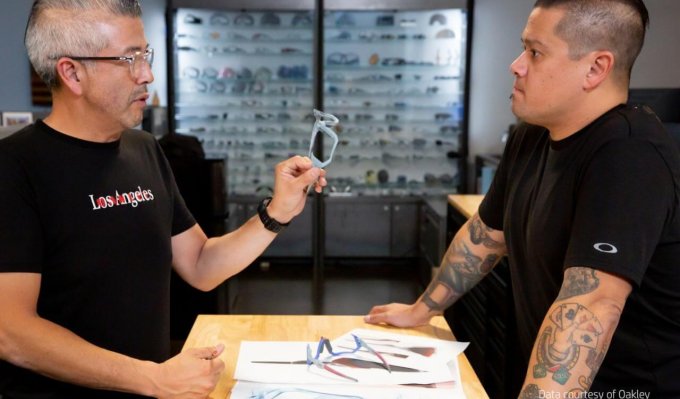 Dva designéři stojí u stolu a prohlíží si barevné obroučky brýlí Oakley vyrobené 3D tiskem