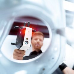 Průhled kulatým otvorem ukazuje 3D skener ZEISS T-SCAN  v rukách operátora se zapnutým laserem