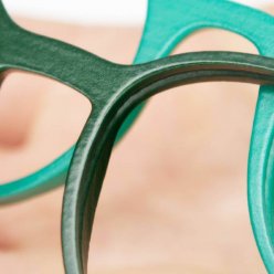 Blízký detail dvou obrouček brýlí v různých odstínech zelené barvy na dřevěné podložce
