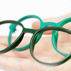 Dvě obroučky brýlí v různých odstínech zelené barvy na dřevěné podložce